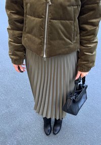 Olive zelenožna pufferska jakna, nabirana bež krila, črne gležnjarje in mala črna torbica s vozelom na ročaju.