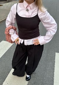 Isik, kellel on seljas roosa nööpidega särk musta sõrmustopiga, mustad laiad püksid, mustad jalatsid valgete sokkidega ja käes roosa scrunchie.