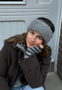 Jeune femme portant un bandeau gris en tricot et des gants rayés, assise dehors près d'une porte blanche, appuyant sa tête sur sa main.