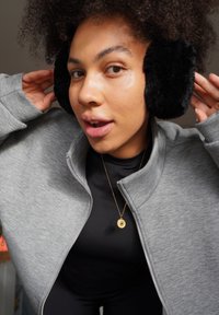 Grey zip-up sweatshirt with high collar, black faux fur earmuffs, and gold circular pendant necklace. Close-up, focus on apparel and accessories.