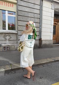 Vit oversized t-shirt med grön text, tillsammans med krämfärgade shorts. Accessoarer inkluderar en mönstrad huvudduk och en virkade väska.