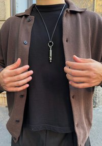 Rudas mezgimo kardiganas virš juodos T-shirt, su mygtukais ir sidabriniu pakabuku ant juodo virvelės. Matoma tekstūruota medžiaga ir laisvas kirpimas.