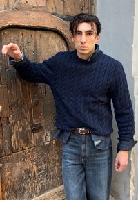 Maglione blu navy a trecce con collo alto, indossato sopra una camicia di jeans, abbinato a jeans a gamba dritta azzurri chiari e una cintura marrone.