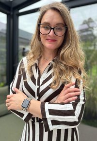Svītrains pogu krekls brūnā un baltā krāsā, ar garām piedurknēm un apkakli. Sudraba metāla pulksteņš uz plaukstas. Gaiša fona ar zaļumiem.