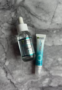 Sérum Hyaluron Aloe Hydro Booster dans un flacon en verre transparent avec compte-gouttes blanc, et stick anti-tâches PureActive dans un tube blanc avec des accents turquoise.