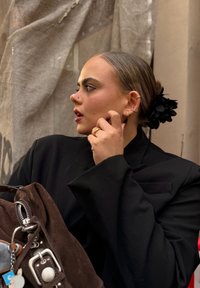 Black oversized blazer with a textured finish, paired with a brown suede bag. Hair styled in a bun adorned with a black floral accessory.
