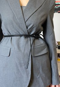 Szary, dopasowany blezer z przednimi kieszeniami, taliowany czarnym paskiem sznurkowym. Gładka faktura i usztywniony krój.