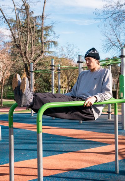 Sudadera gris, pantalones negros y calzado con suelas texturizadas, sobre barras de entrenamiento verdes en un parque con suelo de goma.
