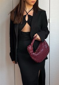 Zwarte bodycon jurk met een zijsplit, gecombineerd met een goed zittende zwarte blazer. Houdt een burgundy gevlochten handtas vast met een zachte, ronde handgreep.