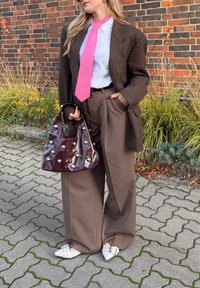 Hnedý vzorovaný oversize blejzer, biela košeľa, ružová kravata, hnedé široké nohavice, lesklá bordová kabelka so striebornými detailmi, biele bodcové topánky.