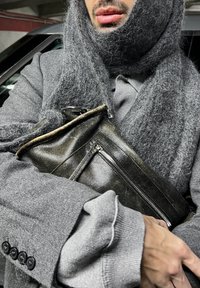 Saco de couro preto com detalhes em zíper, segurado de perto. Cachecol de lã cinza e um casaco cinza com tecido texturizado e detalhes em botão.