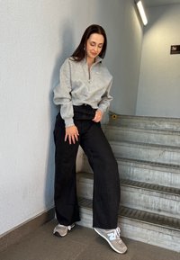 Sivý zipsový sveter, čierne široké nohavice a sivé tenisky na schodoch. Hladká štruktúra, uvoľnený strih a neutrálné odtiene.