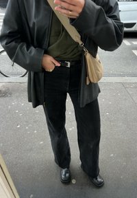 Φαρδιά μαύρα τζιν παντελόνια σε συνδυασμό με ένα σκούρο πράσινο φούτερ, κάτω από μια μακριά μαύρη ζακέτα. Τα αξεσουάρ περιλαμβάνουν μια μικρή μπεζ τσάντα χεριού.