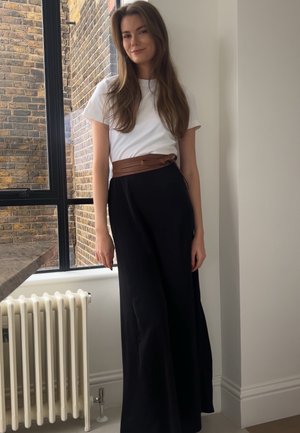 Falda negra con un cinturón envolvente marrón, combinada con una camiseta blanca. La tela parece fluida y suave, con un diseño minimalista.