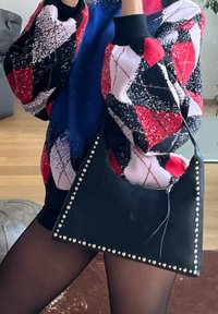 Μαύρη δερμάτινη τσάντα ώμου σε τριγωνικό σχήμα, διακοσμημένη με ασημένιες τρουκς κατά μήκος των ακμών. Λείος υφή με ελαφριά γυαλάδα.