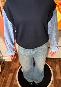 Felpa blu navy con maniche lunghe azzurro chiaro arricciate; abbinata a jeans azzurri a gamba larga. Texture lisce e design stratificato.