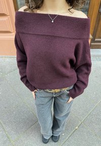 Pull bordeaux à épaules dénudées avec encolure côtelée, associé à un pantalon gris ample et une ceinture à boucle argentée ; tissu texturé, coupe décontractée.