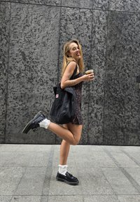 Μαύρο φόρεμα με floral σχέδιο, μαύρη τσάντα ώμου, λευκές γκριτάκια με φουντάκια και μαύρα παπούτσια πλατφόρμας με ασημένιες λεπτομέρειες. Υφή γκρι φόντο.