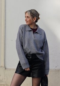Szürke kötött pulóver galléros nyakkivágással, fekete bőrnadrággal párosítva. Az anyag puha, látható bordázott mandzsettákkal és laza fazonnal.