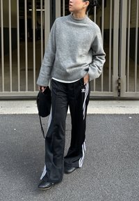 Szürke kötött pulóver kerek nyakkivágással, fekete sportnadrággal fehér oldalsávokkal és Adidas logóval párosítva. Fekete válltáska.