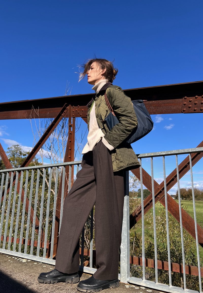 Κουβερτίνα ελαιόχρωμη μπλούζα, κρεμ τζάκετ λαιμόκοψη, καφέ παντελόνι φαρδύ, μαύρα χοντρά παπούτσια, μπλέ τσάντα. Υπαίθρια σκηνικά με γαλάζιο ουρανό.