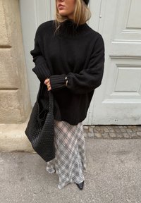 Pull à col roulé noir en maille, coupe ample ; matière texturée. Associé à un sac fourre-tout noir tissé et une jupe à carreaux grise et blanche.