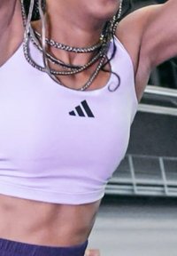 Top deportivo corto de color púrpura claro con escote redondo y logo negro de Adidas en el pecho izquierdo, confeccionado en un material elástico y suave.