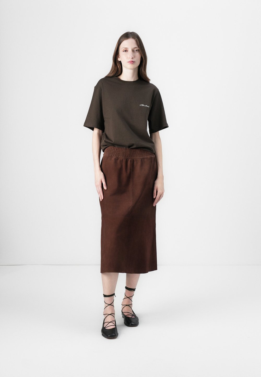 Brown t-shirt with short sleeves and a subtle logo, teamed with a brown midi skirt that has an elastic waistband. Paired with black lace-up flats.