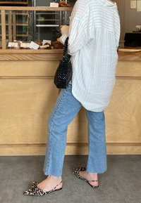 Överdimensionerad vit skjorta med tunna grå ränder; ljusblå utsvängda jeans; svart pärlhandväska; leopardmönstrade ballerinas med rosett.