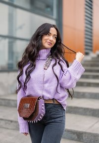Pull en tricot lilas à col montant, jean foncé et sac marron avec texture crocodile et accents à pointes, porté sur l'épaule.