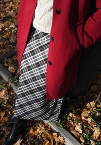 Palton roșu din lână cu nasturi negri, asortat cu o fustă lungă în carouri alb-negru. Botine din piele neagră completează ținuta.