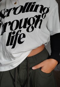 Tricou alb cu text negru "scrolling through life" (derulând prin viață), asortat cu pantaloni verde măsliniu, cu talie elastică și buzunare.