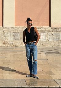 Gilet nero cropped con bottoni, jeans strappati blu chiaro, mocassini a pois bianco e nero, borsa a spalla, davanti a un muro testurizzato.