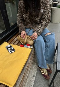 Bundy s leopardím vzorem, světle modré volné džíny s obnošením, hnědé a žluté sneakers, béžová taška, žlutý šátek a vzorovaný kryt na telefon.