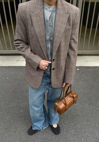 Hnedé kárované sako cez sivé pletené tričko, doplnené širokými modrými džínami, čiernymi topánkami a malou hnedou kabelkou. Textúrovaný, zostrihaný dizajn.