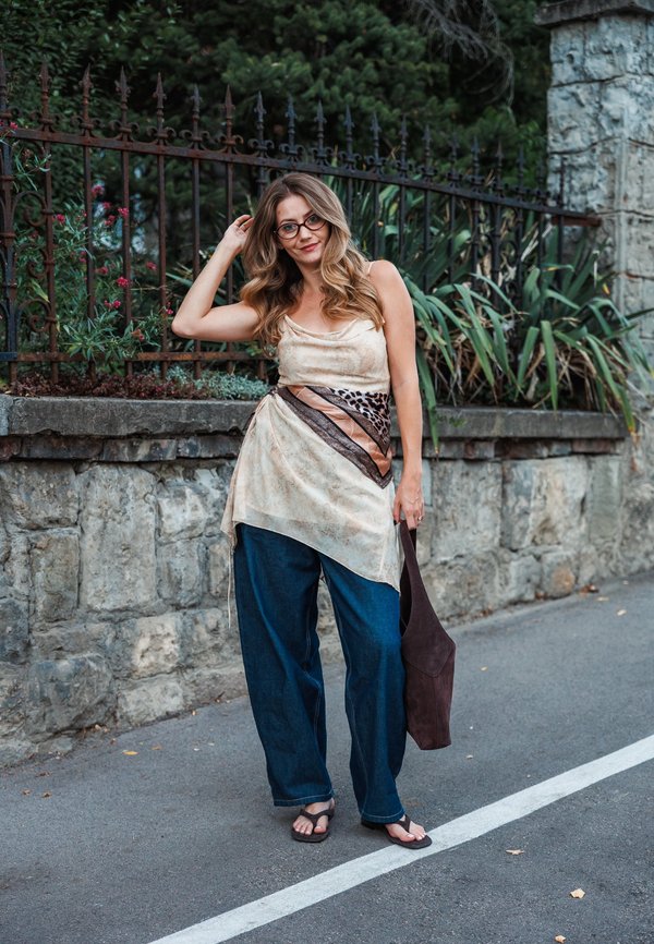 Knee-length, sheer beige top with brown and leopard print accents, paired with wide-leg dark blue denim pants and black flip-flops.