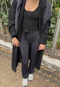 Haut noir à enfiler avec un détail noué, pantalon noir taille haute et long manteau noir, complétés par des baskets blanches. Texturé et ajusté.