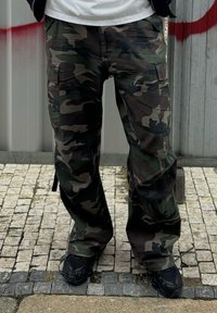 Cargopants mit Tarnmuster, aus robustem Stoff, mit mehreren Taschen, in einer Mischung aus Grün, Braun und Schwarz, lockere Passform.