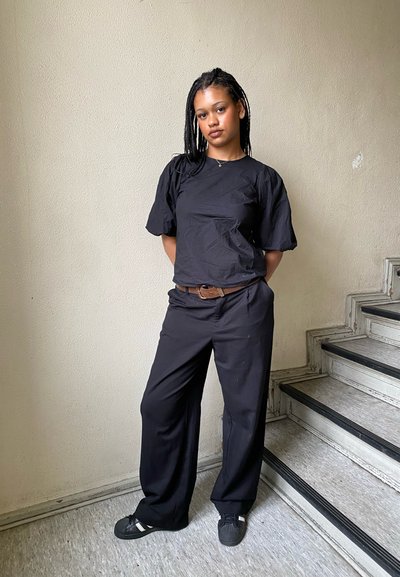 Top negro de manga corta con un corte holgado, combinado con pantalones anchos negros y zapatos negros sin cordones. La textura es suave y mate.