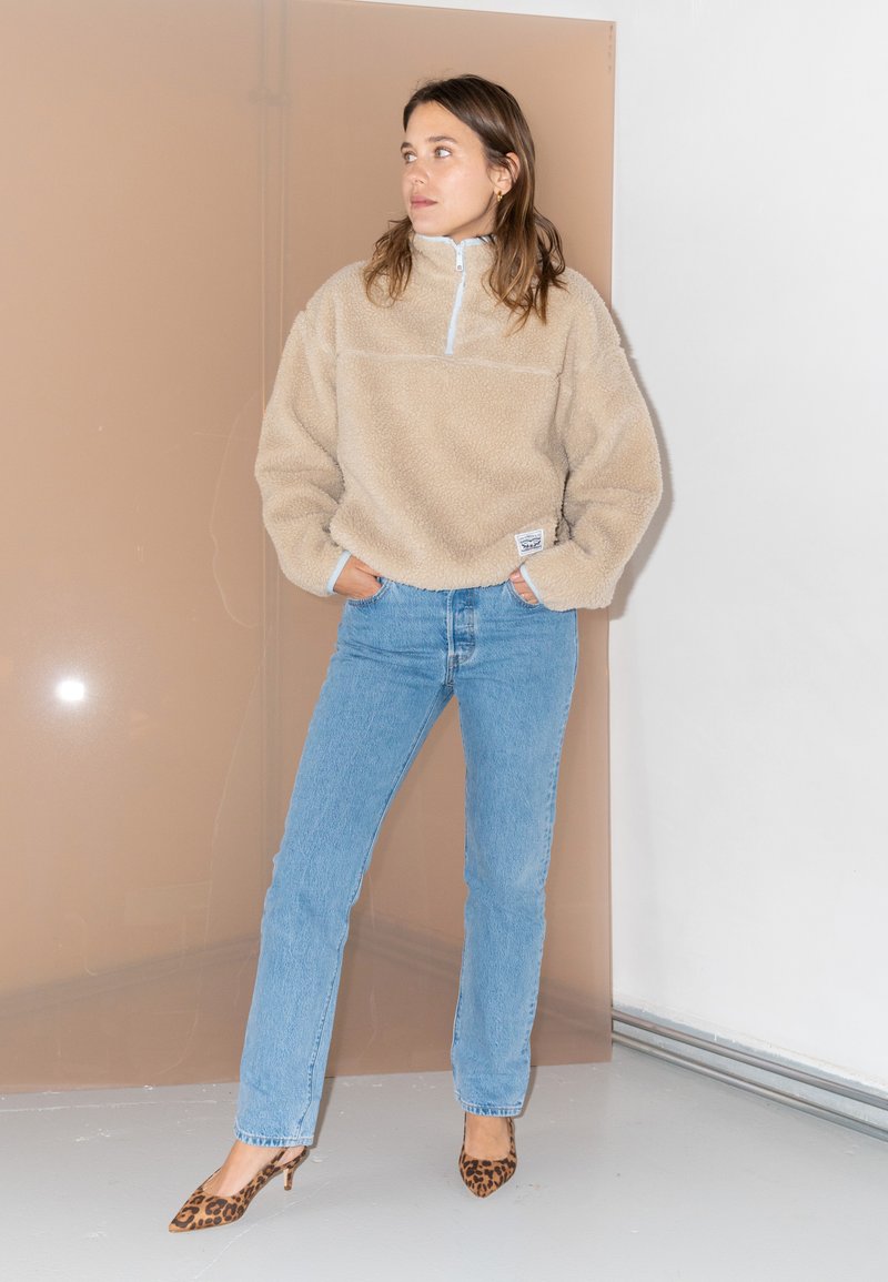 Beige fleece-pullover med halv lynlås og en lomme. Parret med lyseblå lige ben-jeans og brune leopardprint hæle.