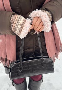 Sac à main noir en cuir embossé crocodile avec deux poignées et une fermeture éclair. Orné d'une écharpe à franges rose et de manches tricotées avec un bord duveteux.