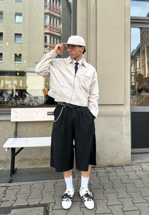 Šviesiai ruda trumpa striukė su užtrauktuku priekyje, derinama su juodomis kelnių ilgio šortais. Baltos kojinės ir juodi bei balti sportbačiai užbaigia įvaizdį.