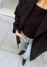 Czarna, oversize'owa marynarka, dopasowany czarny top i jasnoniebieskie dżinsy. Czarne, spiczaste botki za kostkę. Gładki materiał i strukturalny krój.
