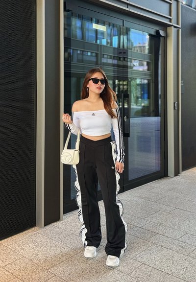 Top corto blanco sin mangas con rayas negras, combinado con pantalones de chándal negros que tienen detalles de volantes blancos a los lados. Gafas de sol negras y bolso.