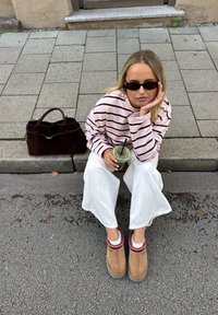 Brun ruskindstaske, lyserød og sort striped langærmet skjorte, hvide bukser med vide ben, brune støvler med rødt kantbånd og grøn drik med sugerør.