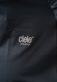 Logo Ciele Athletics wydrukowane na czarnym materiale w kolorze białym, z widocznymi szwami i delikatnymi zmarszczkami.