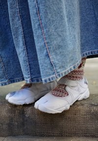 Baskets blanches à bouts fendus portées avec des chaussettes rouges à motifs sous une longue jupe en jean bleu sur une marche en pierre en plein air.