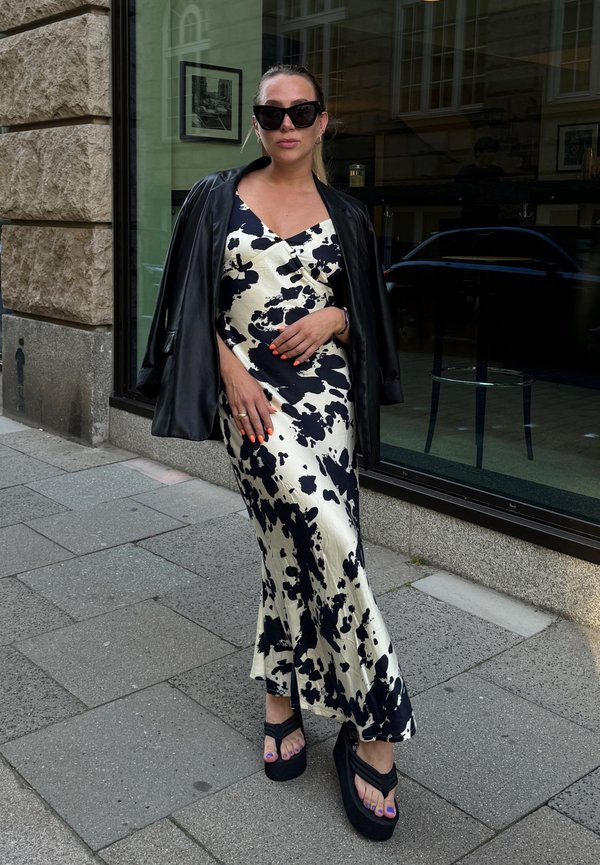 Das Kleid hat ein schwarz-weißes Kuhmuster, eine satinähnliche Textur und eine taillierte Silhouette. Kombiniert mit schwarzen Plateausandalen und einer Lederjacke.