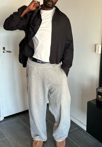 Veste noire courte portée sur un t-shirt blanc, associée à un pantalon de survêtement gris clair avec une ceinture noire, et des bottines beige.