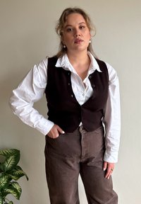 Brown wool waistcoat over a white collared shirt, paired with light brown high-waisted trousers. Features button detailing and a relaxed fit.